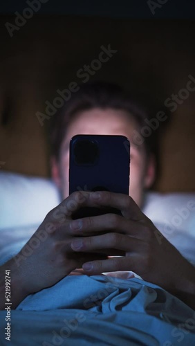 Vertical Screen: Caucasian Man Uses Smartphone in Bed at Home at Night. Handsome Guy Browsing Social Media, Reading News, Doing Online Shopping, Late at Night. Holding Mobile Phone