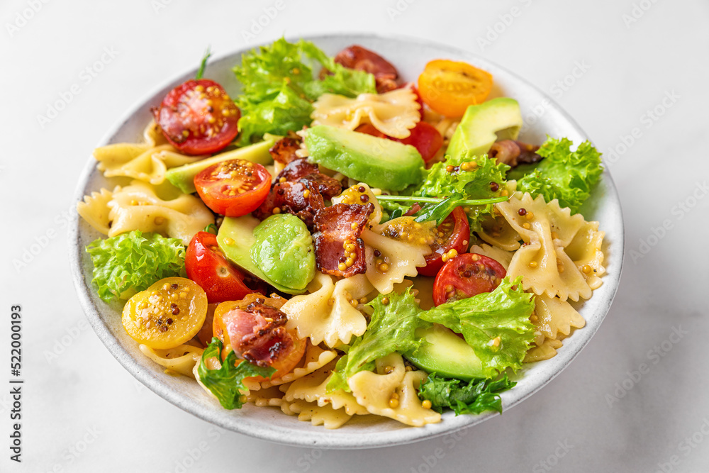 Pasta farfalle salad with tomato, bacon, avocado and mustard dressing in a plate on white table. Close up Pasta farfalle salad with tomato, bacon, avocado and mustard dressing in a plate on white table. Close up