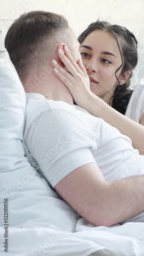 vertical video of happy brunette woman touching face of boyfriend while lying on bed