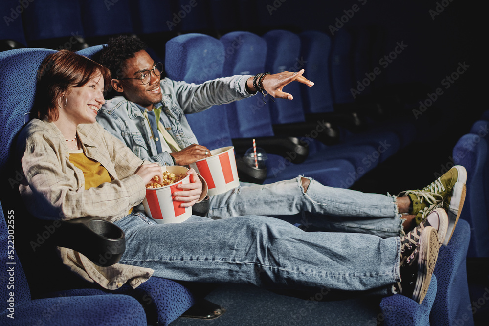 Young gen Z African American man and Caucasian woman in love wearing casual clothes enjoying watching action movie at cinema