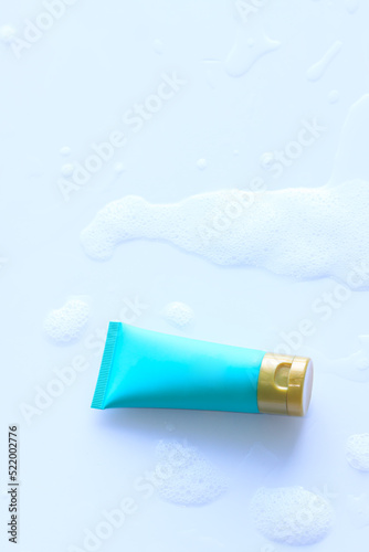 Blue cosmetic bottle shower gel on plastic board with foam bubbles background in the bathroom