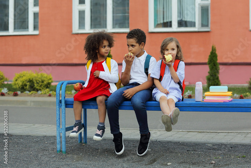 Cute Black schoolboy and girls are eating outdoors next the school.