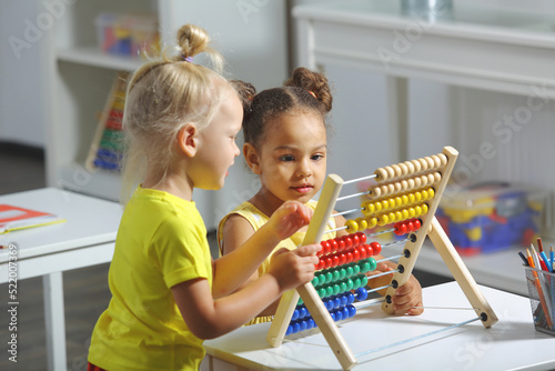 children of different races sit together at the table and count on the abacus