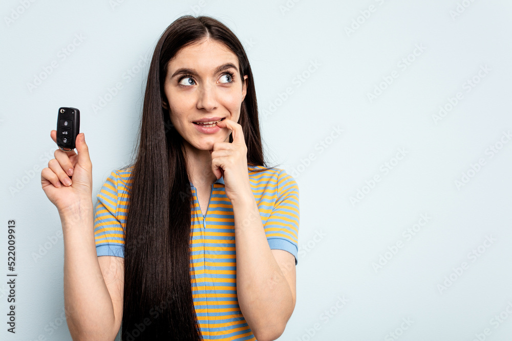 Young caucasian woman holding car keys isolated on blue background relaxed thinking about something looking at a copy space. Young caucasian woman holding car keys isolated on blue background relaxed thinking about something looking at a copy space.
