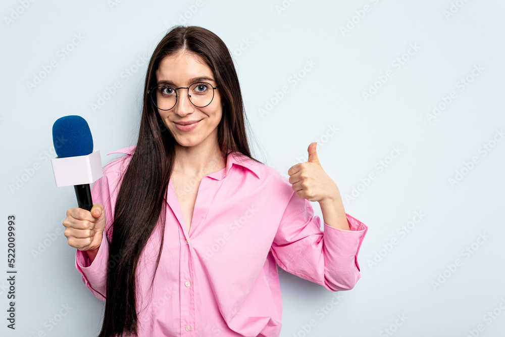 Young caucasian tv presenter woman isolated on blue background smiling and raising thumb up Young caucasian tv presenter woman isolated on blue background smiling and raising thumb up