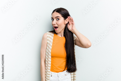 Young caucasian woman isolated on white background trying to listening a gossip.