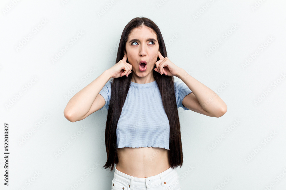Young caucasian woman isolated on white background covering ears with fingers, stressed and desperate by a loudly ambient.