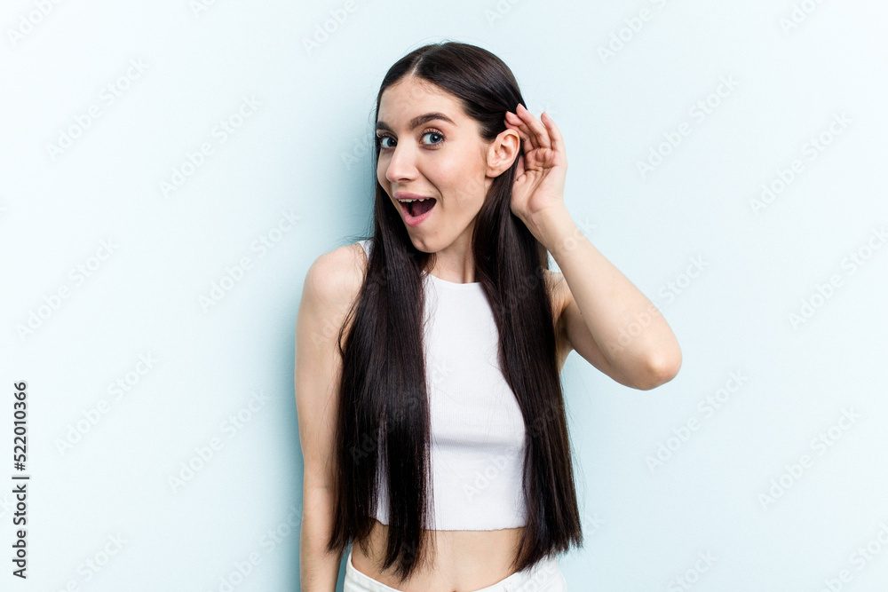 Young caucasian woman isolated on blue background trying to listening a gossip.