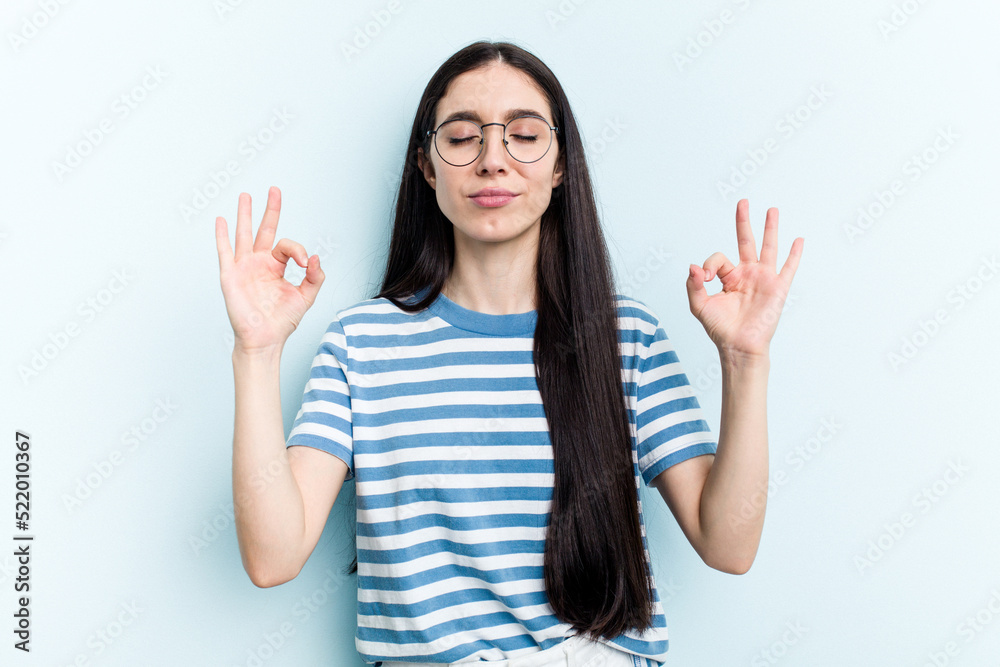 Young caucasian woman isolated on blue background relaxes after hard working day, she is performing yoga. Young caucasian woman isolated on blue background relaxes after hard working day, she is performing yoga.