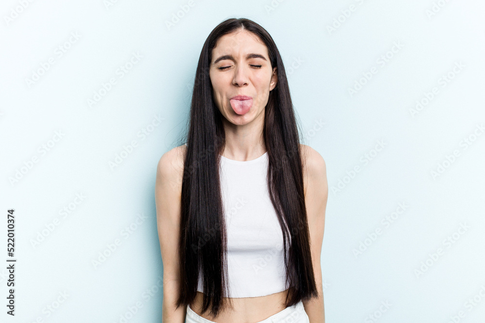 Young caucasian woman isolated on blue background funny and friendly sticking out tongue. Young caucasian woman isolated on blue background funny and friendly sticking out tongue.