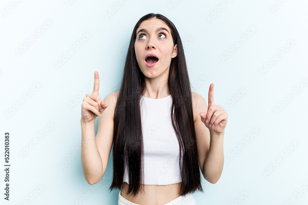 Young caucasian woman isolated on blue background pointing upside with opened mouth.