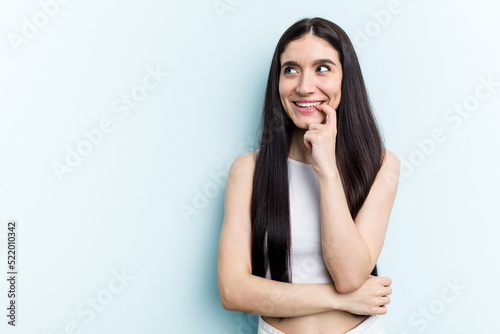 Young caucasian woman isolated on blue background relaxed thinking about something looking at a copy space. © Asier