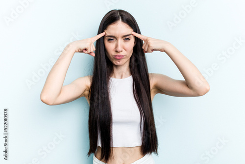 Young caucasian woman isolated on blue background focused on a task, keeping forefingers pointing head.