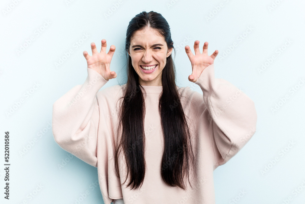 Young caucasian woman isolated on blue background showing claws imitating a cat, aggressive gesture. Young caucasian woman isolated on blue background showing claws imitating a cat, aggressive gesture.