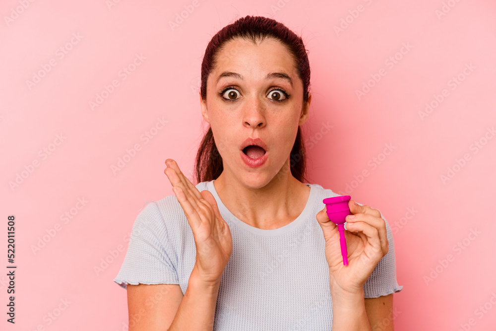 Young caucasian woman holding a menstrual cup isolated on pink background surprised and shocked. Young caucasian woman holding a menstrual cup isolated on pink background surprised and shocked.