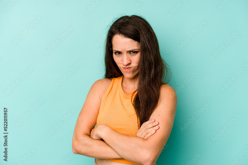 Young caucasian woman isolated on blue background frowning face in displeasure, keeps arms folded.