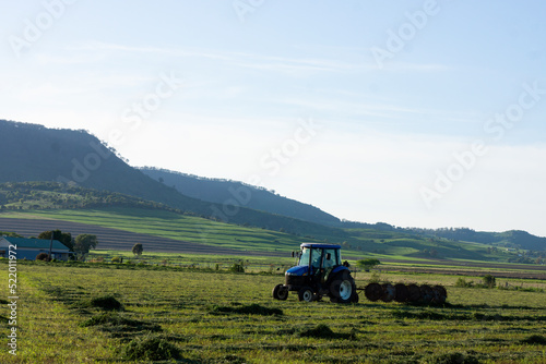 Man on his tractor raking hay against a backdrop of lush countryside in Southern Queensland on a hazy early morning.