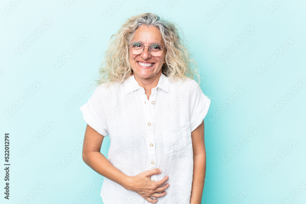 Middle age caucasian woman isolated on blue background touches tummy, smiles gently, eating and satisfaction concept. Middle age caucasian woman isolated on blue background touches tummy, smiles gently, eating and satisfaction concept.