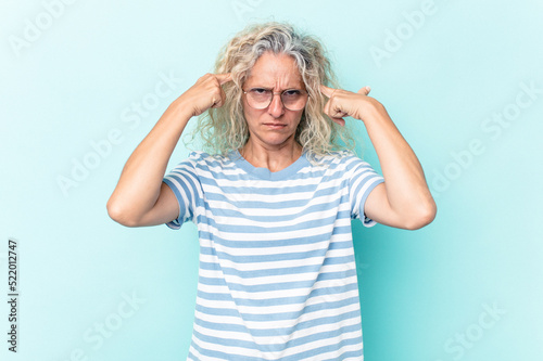 Middle age caucasian woman isolated on blue background focused on a task, keeping forefingers pointing head.