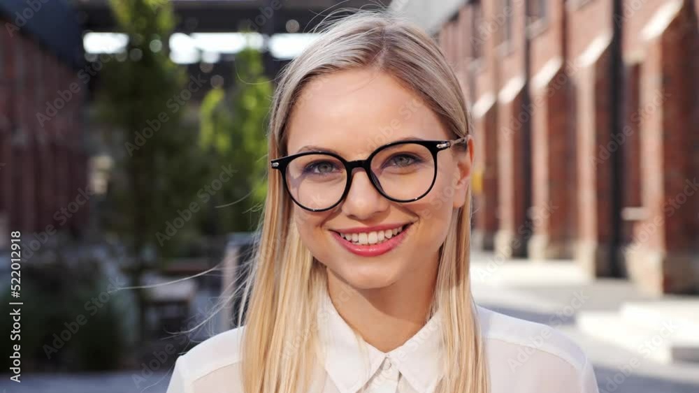 Young positive female blonde blogger standing outdoors greeting subscriber start speech looks at camera. Job interview activity, distant communication using video conference application concept. Young positive female blonde blogger standing outdoors greeting subscriber start speech looks at camera. Job interview activity, distant communication using video conference application concept.