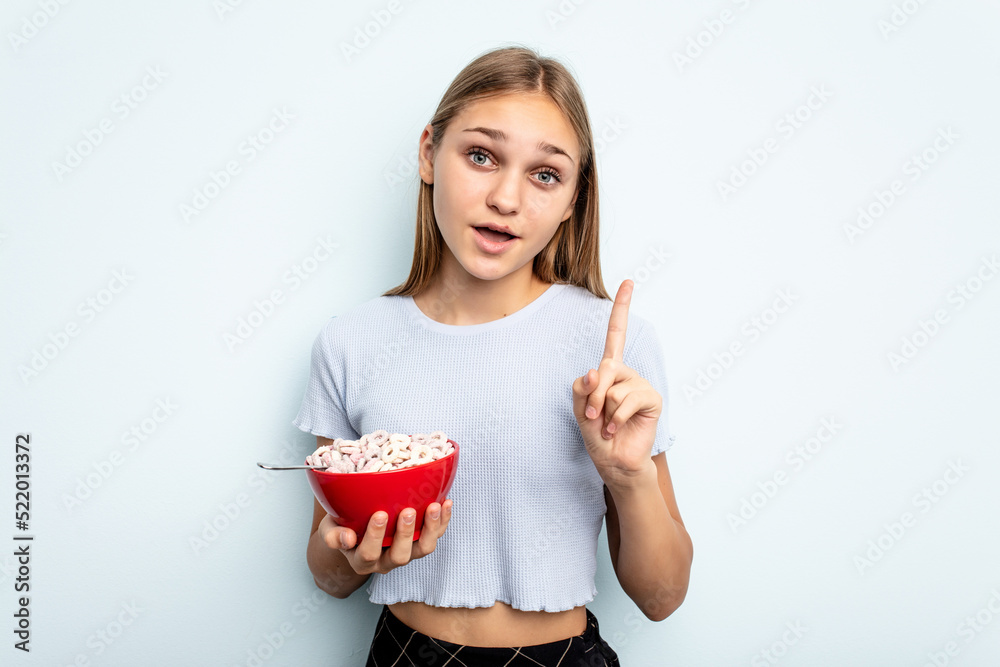 Young caucasian girl eating cereals isolated on blue background having an idea, inspiration concept. Young caucasian girl eating cereals isolated on blue background having an idea, inspiration concept.
