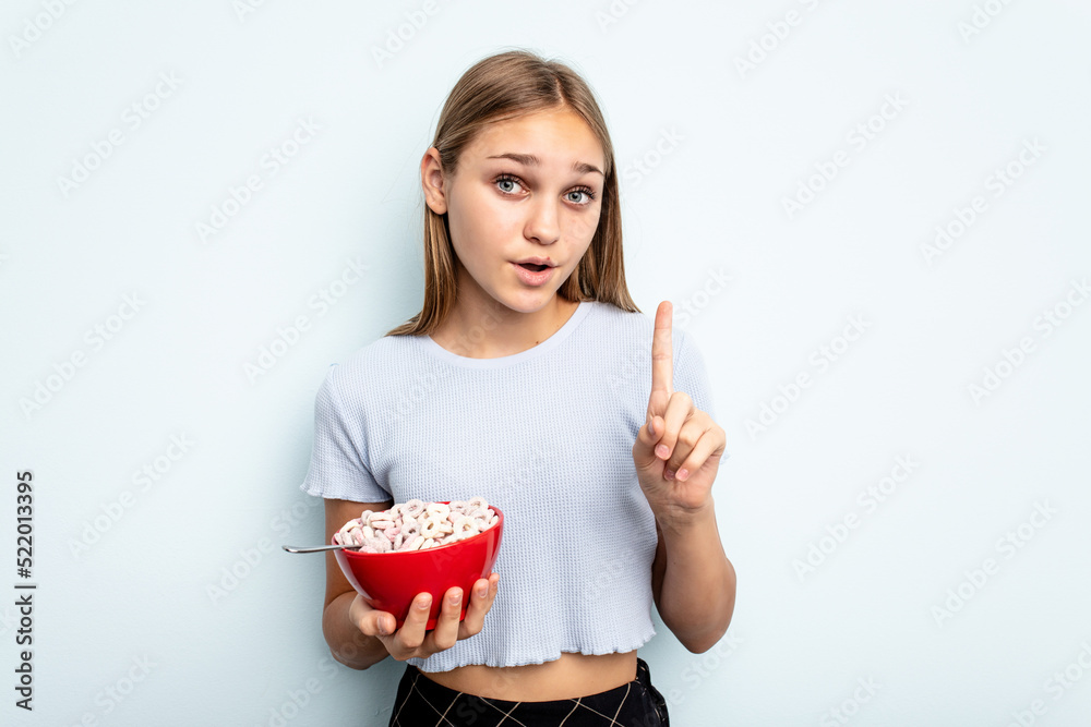 Young caucasian girl eating cereals isolated on blue background having some great idea, concept of creativity. Young caucasian girl eating cereals isolated on blue background having some great idea, concept of creativity.