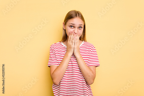 Young caucasian girl isolated on yellow background shocked covering mouth with hands.
