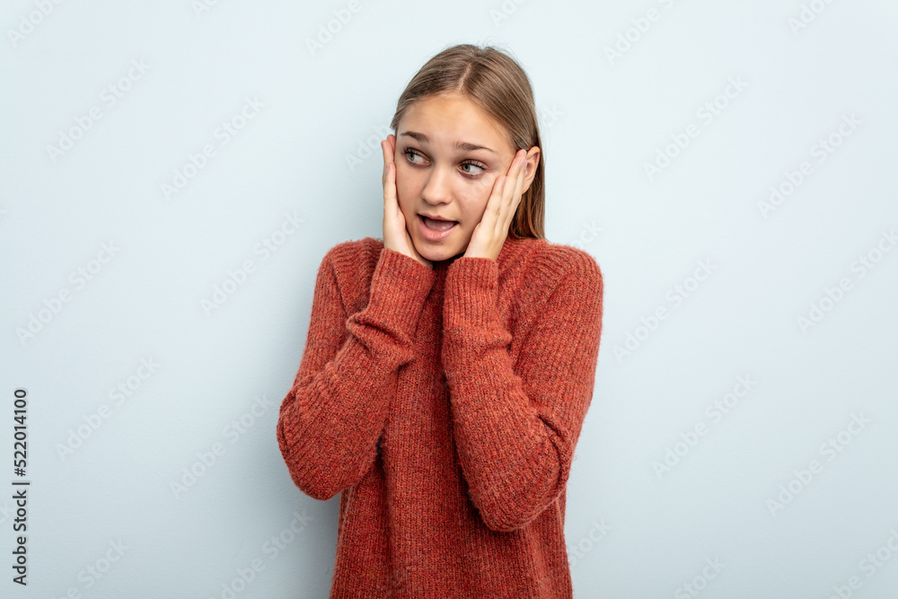 Young caucasian girl isolated on blue background covering ears with hands trying not to hear too loud sound. Young caucasian girl isolated on blue background covering ears with hands trying not to hear too loud sound.