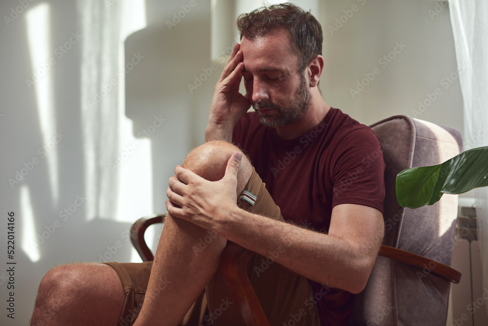 Man with headache sitting in chair at home.