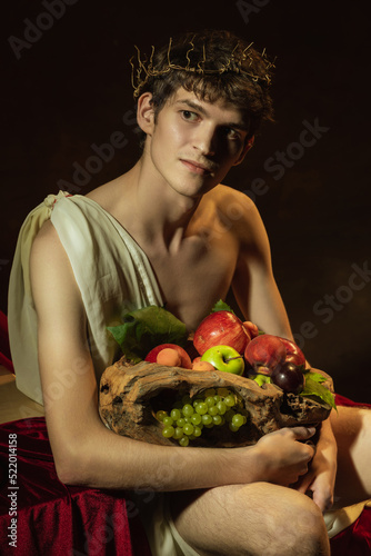 Creative remake of painting boy with a basket of fruit. Young handsome man over dark vintage background. Italian baroque style, art, creativity, vintage photo