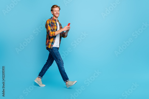 Full length photo of handsome guy with ginger hair wear plaid shirt holding smartphone online shopping isolated on blue color background