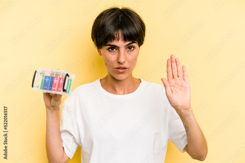 Young caucasian woman holding a batteries box isolated on yellow background standing with outstretched hand showing stop sign, preventing you. Young caucasian woman holding a batteries box isolated on yellow background standing with outstretched hand showing stop sign, preventing you.