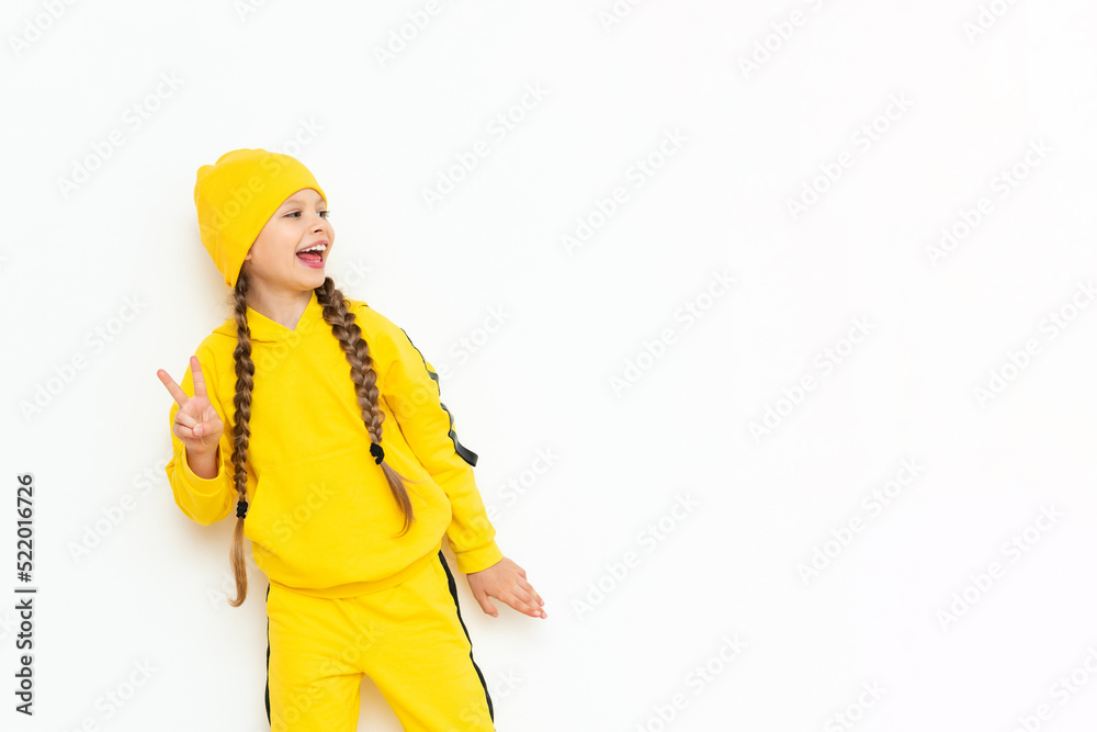 A little girl in a hat and a yellow suit points to your advertisement on a white isolated background. Autumn clothes for children. Copy space.
