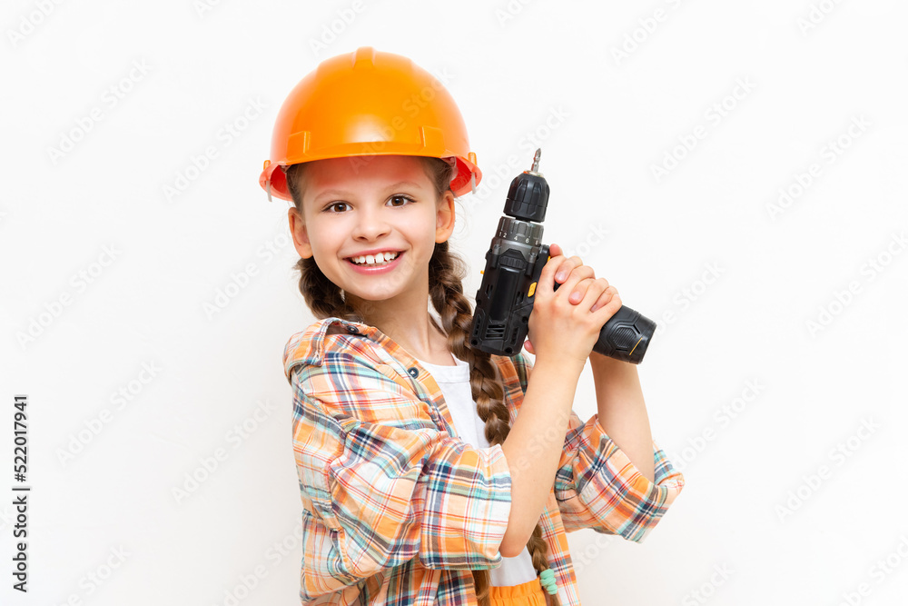 A little girl with an electric screwdriver in a protective orange construction helmet smiles broadly on a white isolated background. The concept of renovation in the room of a teenage girl. A little girl with an electric screwdriver in a protective orange construction helmet smiles broadly on a white isolated background. The concept of renovation in the room of a teenage girl.