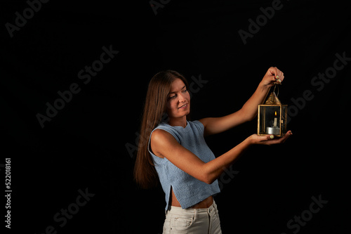 young woman lit by old lantern with candle on black background