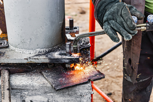 Worker cutting metal plate by Gas Cutting Torch at a construction site. Installation of a metal structure. Close-up. The welder performs the installation of metal structures. Sparks from welding.