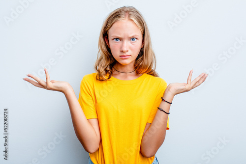 Caucasian teen girl isolated on blue background doubting and shrugging shoulders in questioning gesture. © Asier