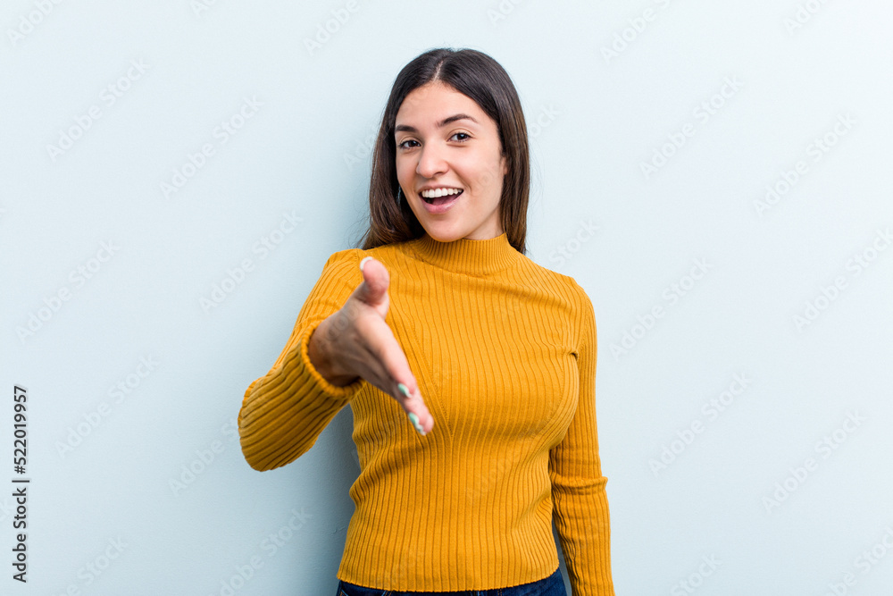 Young caucasian woman isolated on blue background stretching hand at camera in greeting gesture. Young caucasian woman isolated on blue background stretching hand at camera in greeting gesture.
