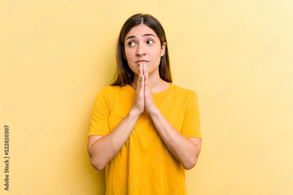 Young caucasian woman isolated on yellow background praying, showing devotion, religious person looking for divine inspiration. Young caucasian woman isolated on yellow background praying, showing devotion, religious person looking for divine inspiration.
