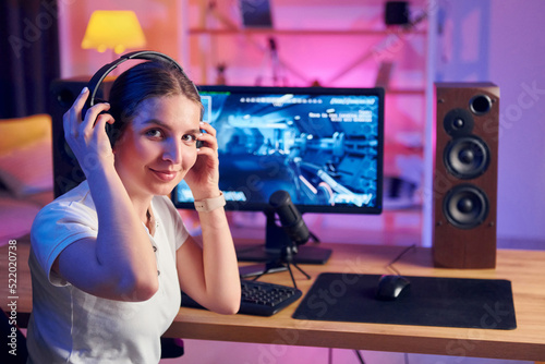 Wearing headphones. Young woman streaming online FPS shooter game at home