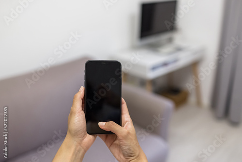 The concept of smart home and smart home control. Close-up of smartphone screen with blank screen mockup for smart home control system interface on interior background. Healthy indoor climate.
