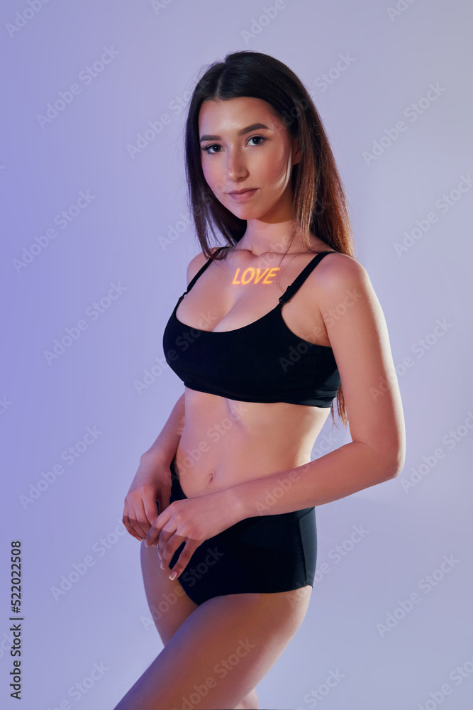 Standing with hands on the waist. Beautiful young woman is in projector neon lights in the studio Standing with hands on the waist. Beautiful young woman is in projector neon lights in the studio