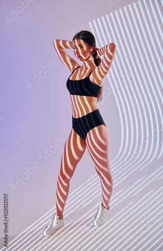 Standing and posing. Beautiful young woman is in projector neon lights in the studio