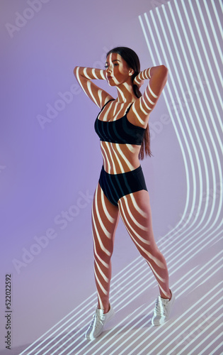 Standing and posing. Beautiful young woman is in projector neon lights in the studio