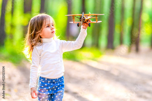 Little girl playing with a yellow airplane in the forest