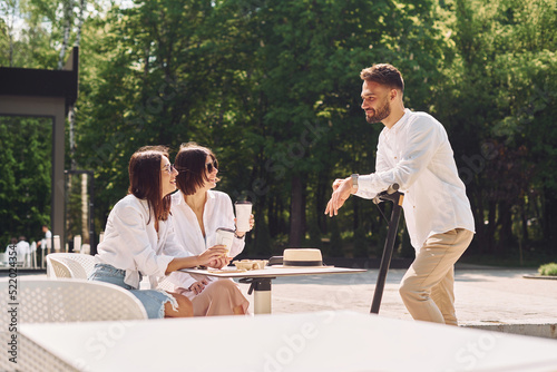 Man is with a scooter. Three friends having great weekend outdoors together