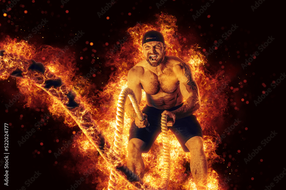 Muscular man working out with battle ropes. Flame background