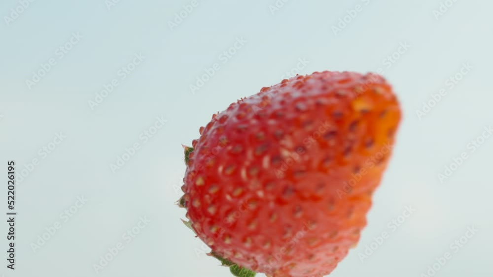 Half a strawberry rotates against the background of the blue sky, close-up. Half a strawberry rotates against the background of the blue sky, close-up.