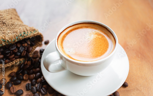 Close-up of a cup of latte with golden foam and mixed or blend coffee beans in a brown sack on an old wooden floor, top view. photo