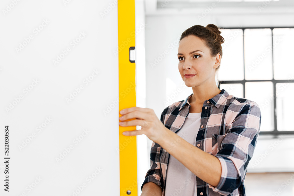 repair, construction and building concept - happy smiling woman with level measuring wall at home repair, construction and building concept - happy smiling woman with level measuring wall at home
